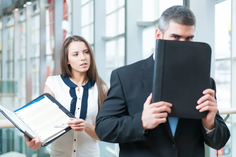 Businessman hiding from a coworker behind a folder