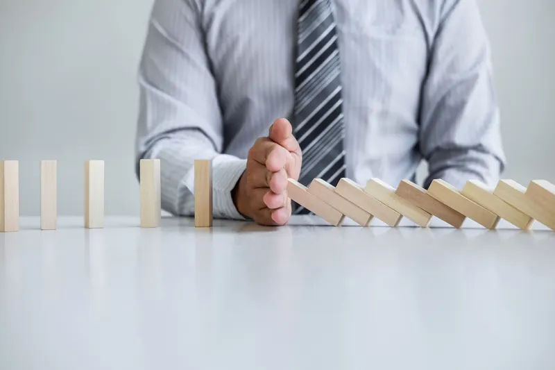 Planning risk and strategy in business: a businessman's hand stopping falling wooden dominoes to prevent a chain reaction