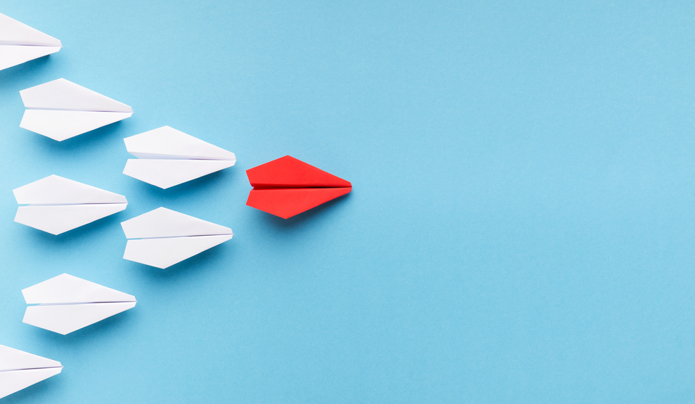 One blue paper plane leading group of white ones